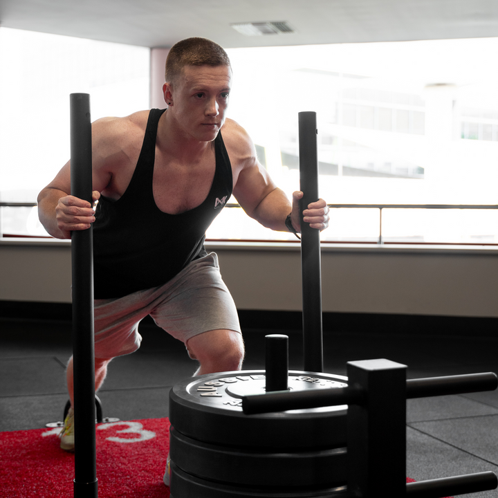 IXK Gear Stringer Tank Top in Colour: Black. Gym Background. Model is also wearing IXK Gear Cotton Stretch Shorts in Grey