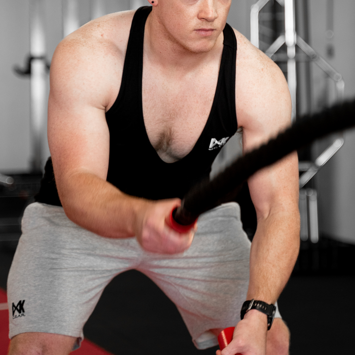 IXK Gear Stringer Tank Top in Colour: Black. Gym Background. Model is also wearing IXK Gear Cotton Stretch Shorts in Grey