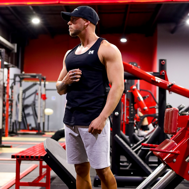 IXK Gear Muscle Tank Top in Black paired with Cotton Stretch Shorts in Grey. Gym background.