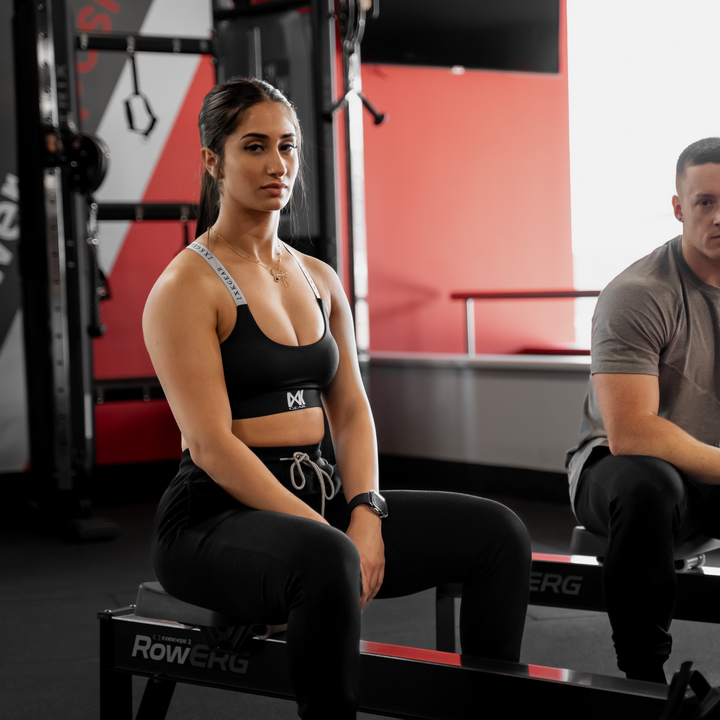 IXK Gear X Sports Bra in Colour: Black. Model is also wearing Cropped Trackies in Colour: Black Gym Background.