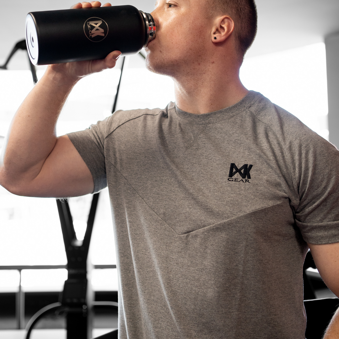 IXK Gear Cotton Tee in Grey. Model is holding the IXK Gear Hot and Cold Bottle in 1l. Gym Background.