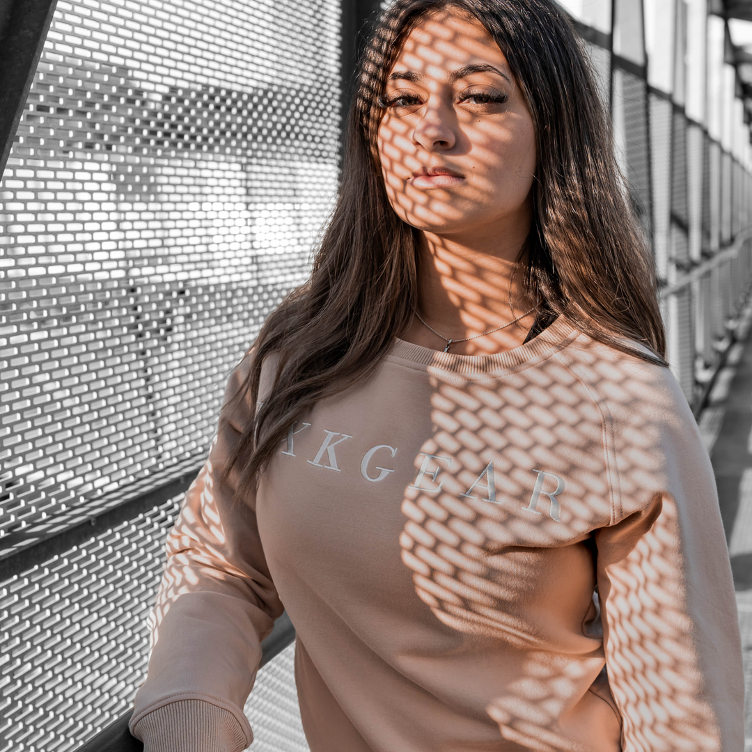 IXK Gear Crewneck Jumper in colour: Sand. Metal grate background and shadow on model face.