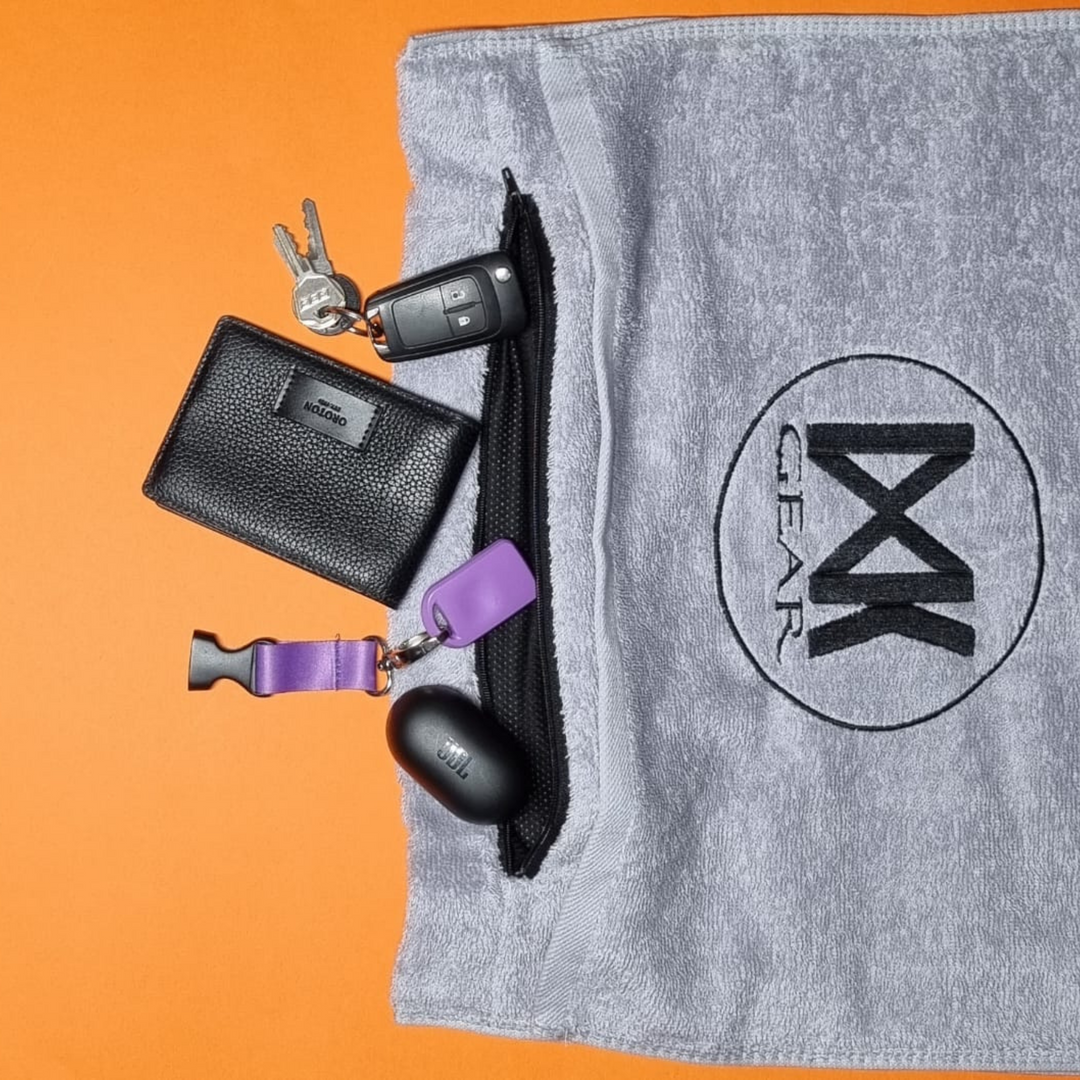 IXK Gear Gym Towel in Grey demonstrating the zip pocket with essentials. Plain orange background.