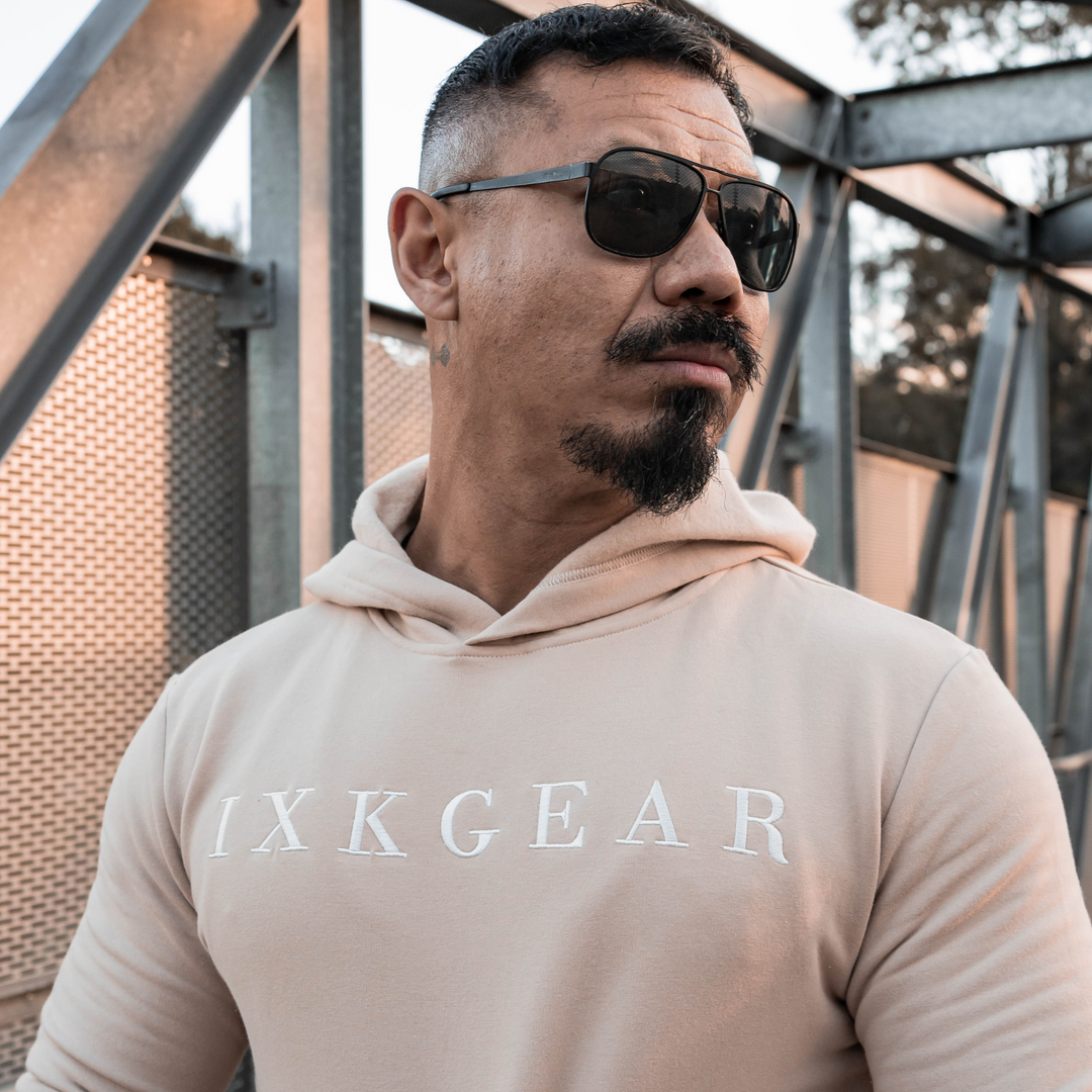 Male model is wearing the IXK Gear Muscle Hoodie in Colour: Sand. Metal Mesh background.