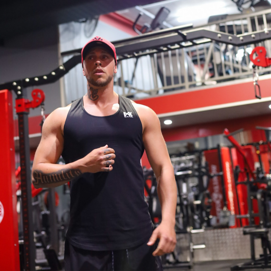 Male model wearing Muscle Tank Top in Black. Gym background.