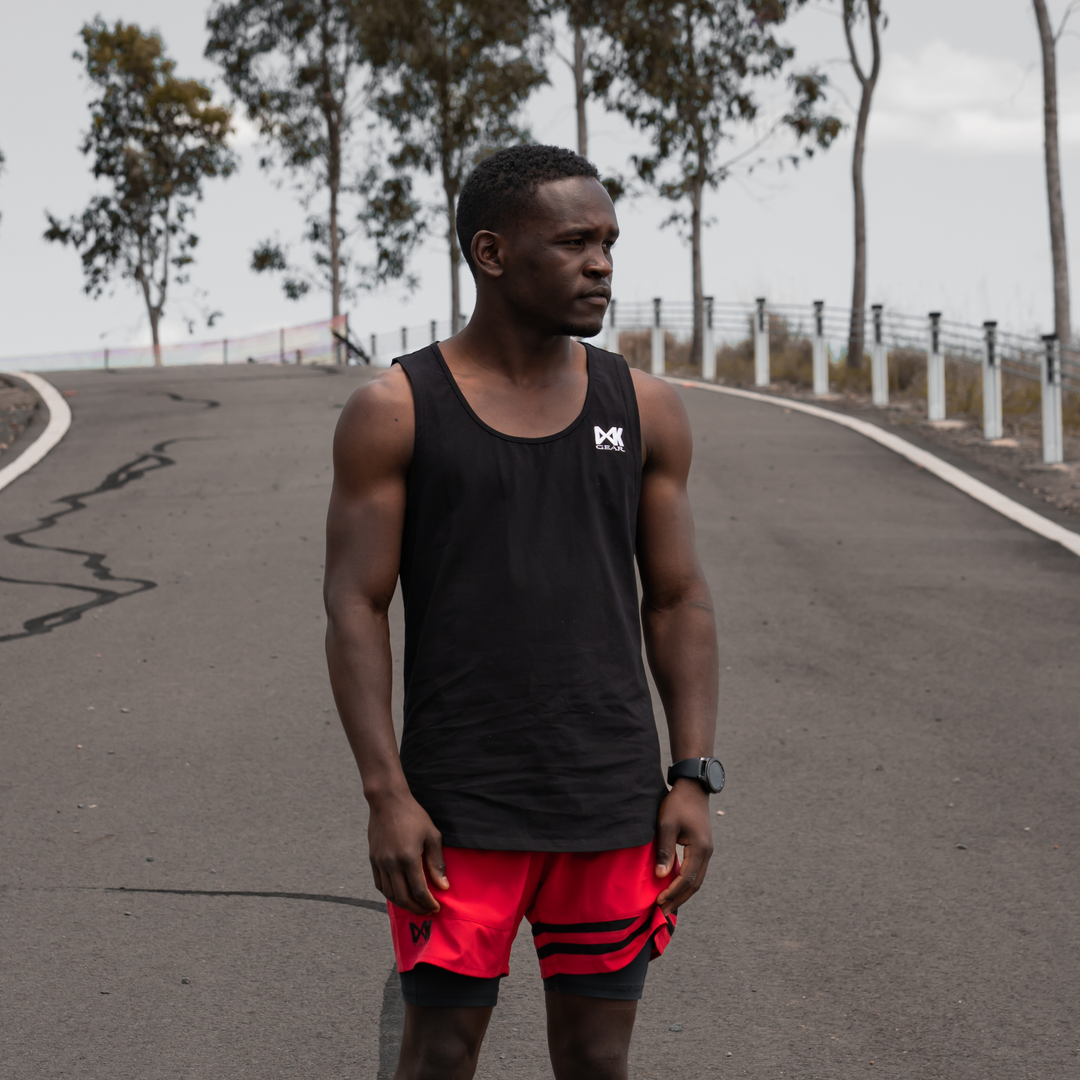 IXK Gear Muscle Tank Top in Black paired with Quick Dry Accent Shorts in Red. Natural road background.