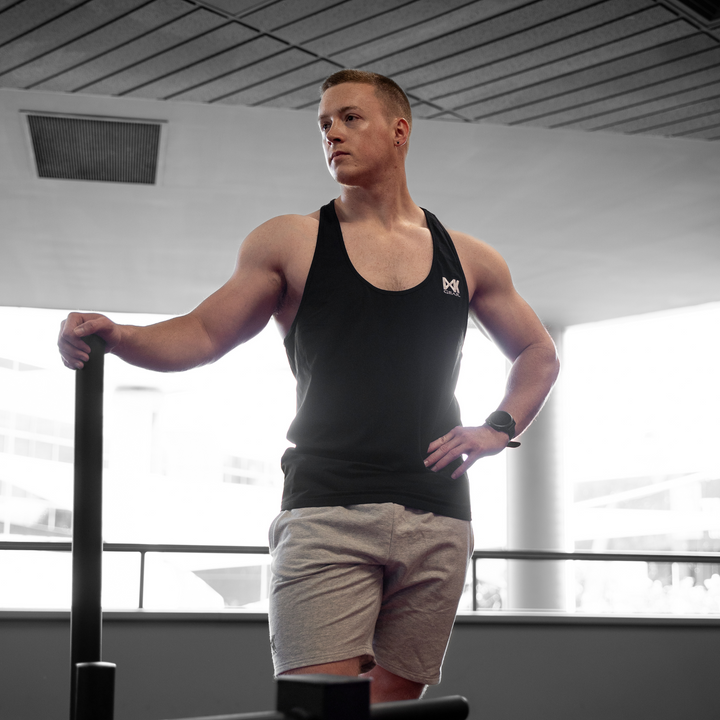 IXK Gear Stringer Tank Top in Colour: Black. Gym Background. Model is also weaaring IXK Gear Cotton Stretch Shorts in Grey