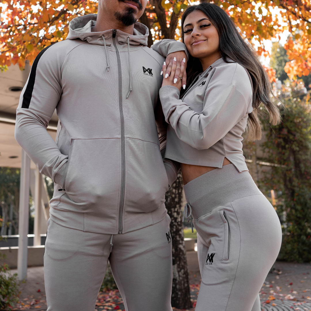 IXK Gear Women's Tracksuit in colour: Stone. Two-Piece tracksuit which includes slightly cropped hoodie and slim-fit trackpants trackies with zip pockets. Natural background. Male model is wearing the IXK Gear Men's Tracksuit in Stone.