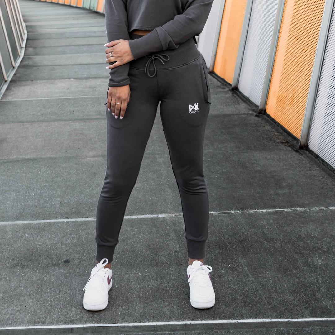 IXK Gear Women's Tracksuit in colour: Charcoal. Two-Piece tracksuit which includes slightly cropped hoodie and slim-fit trackpants trackies with zip pockets. Orange mesh background. Close up shot of the trackpants.