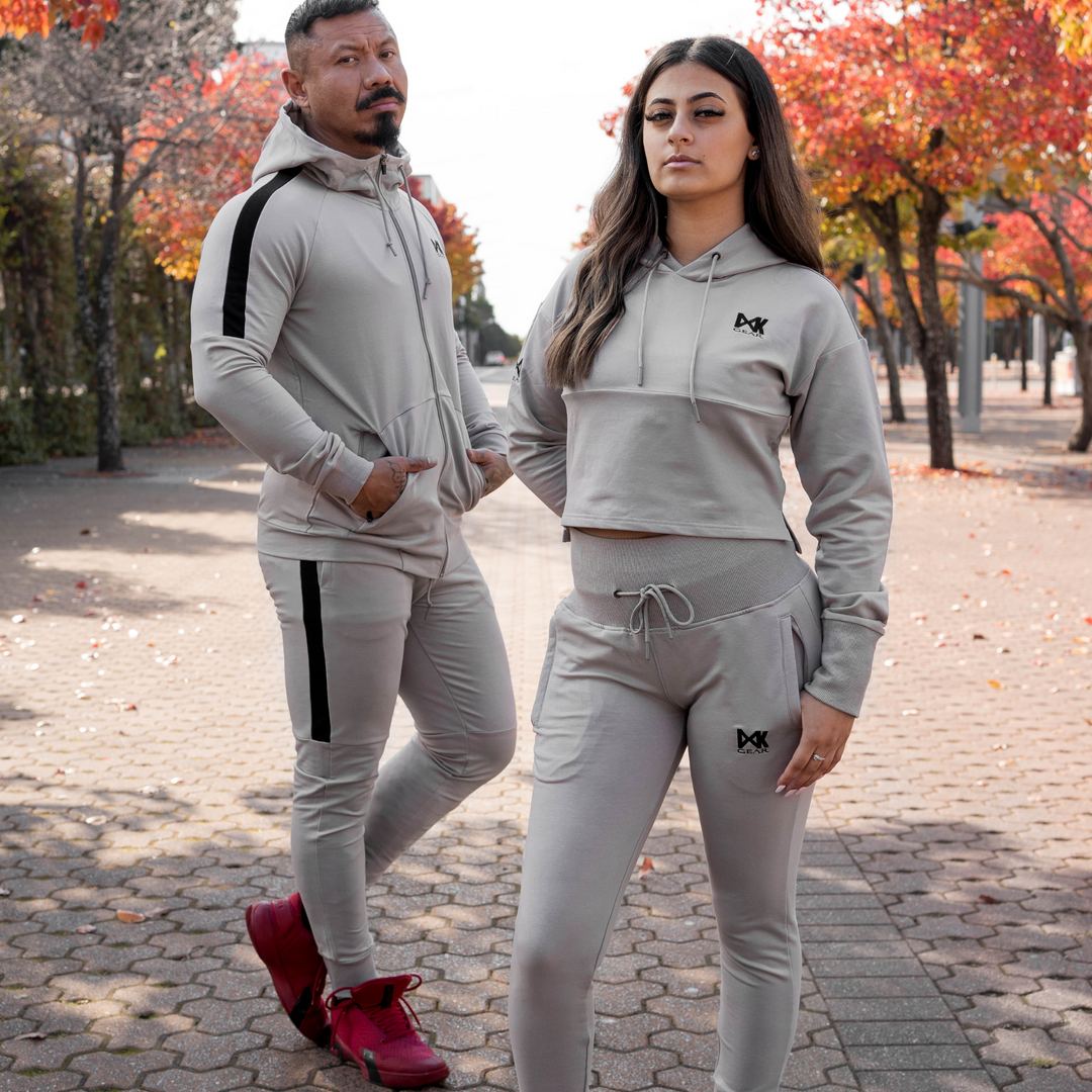 Model is wearing the complete IXK Gear Men's Tracksuit in Colour: Stone. Tree and pavement Background. Female model is wearing the complete IXK Gear Women's Tracksuit in Colour: Stone