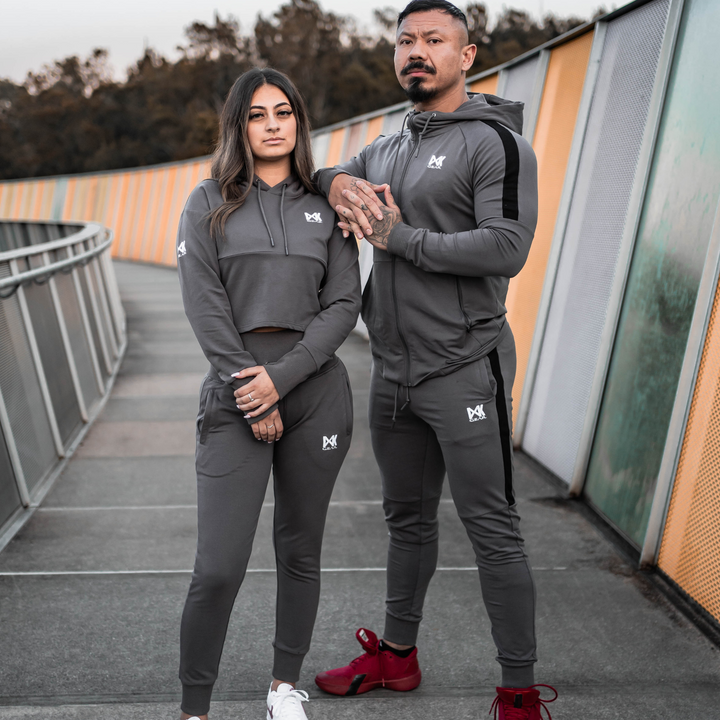 Model is wearing the complete IXK Gear Men's Tracksuit in Colour: Charcoal. Metal Mesh Background. Female model is wearing the complete IXK Gear Women's Tracksuit in Colour: Charcoal